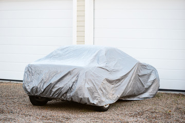 Sports car under silver colored cover outside a closed garage. - 132058714