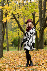 Woman in a floral patterned coat and wine red hat in the park. Happy girl and colorful autumn forest. Portrait of a lady, yellow, green, red and brown leaves background