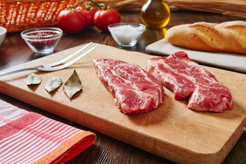 Kitchen table with raw meat on cutting board and ingredients