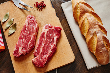 Raw meat on wooden cutting board surrounded by red pepper and bread