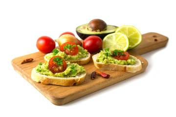 Canapes with avocado cream or guacamole, tomatoes and ingredients on a wooden board, isolated on white