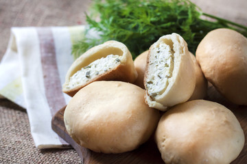 Pies with salty cottage cheese and greens on a wooden board