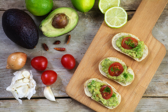 avocado cream or guacamole on baguette canapes and ingredients on rustic wood from above