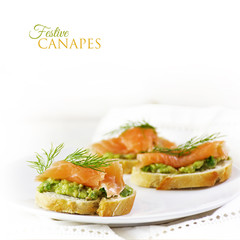 Baguette slices with smoked salmon and avocado cream or guacamole, text festive canapes