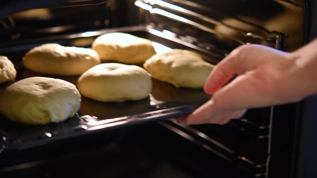 A female hand puts a baking tray with handmade bread inside a home oven.