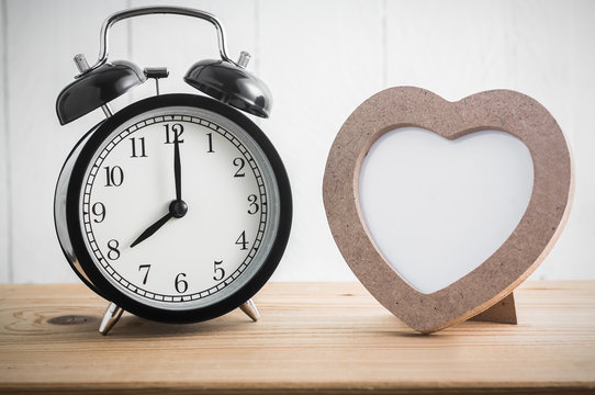 Heart shaped photo frame with clock on wood table