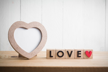 Heart shaped photo frame with "love" in cube on wood table