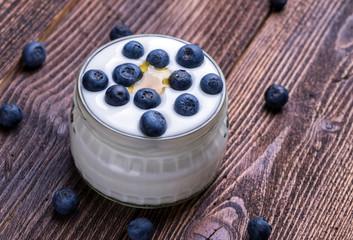 White yogurt in glass bowl with whole blueberries on wooden rustic table. Closeup detail.