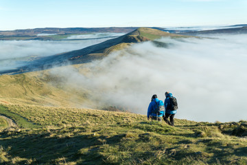 Male and female hikers walk along the great ridge along from Mam Tor, Peak District, Hope Valley on a cold winter morning