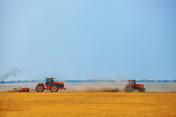 Obraz premium Summer day two tractors to plow, plow the soil on sloping, cornfield. Agricultural land treatment before planting.