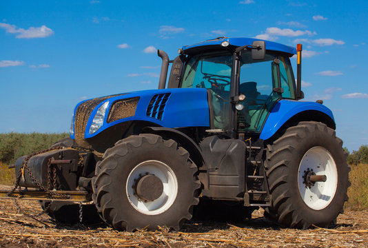 Large new blue tractor plowing a field after harvest on a sunny day. The work of agricultural machinery.