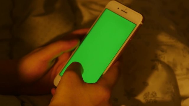 A man uses a green screen smart phone on bed