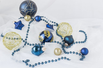 horizontal image of dark blue Christmas balls of different sizes along with gold wire balls scattered through out the image with blue swing of beads placed around them on white background