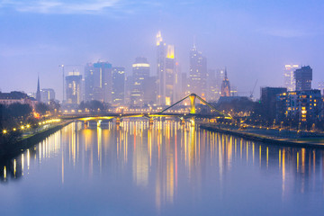 Fototapeta na wymiar Picturesque view of foggy Frankfurt am Main skyline during evening blue hour with mirror reflections in the river, Germany