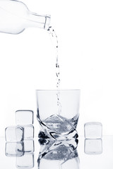 Glass with water, bottle, splash, and ice cubes