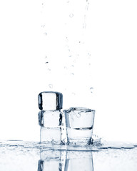 Glass with transparent liquid with ice cubes, splashes and drops