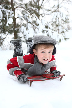 Young boy playing in the snow on an old fashioned sled