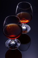 Two glasses of brandy on a dark background with reflection