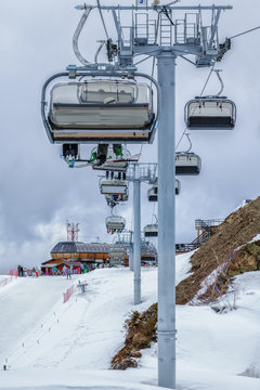 Skiers and snowboarders being transported on a chair ski lift in Sochi mountain ski resort on a cloudy winter day. Vertical landscape