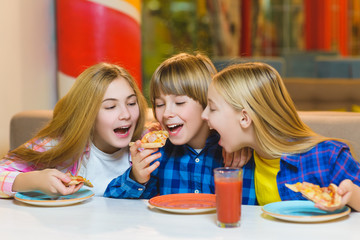 smiling boy and girls eating pizza or drinking juice indoor