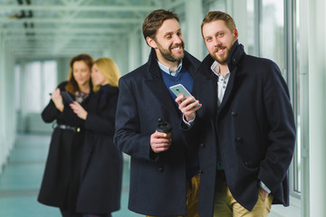 Two businessman holding smart phone in lobby with colleagues at background