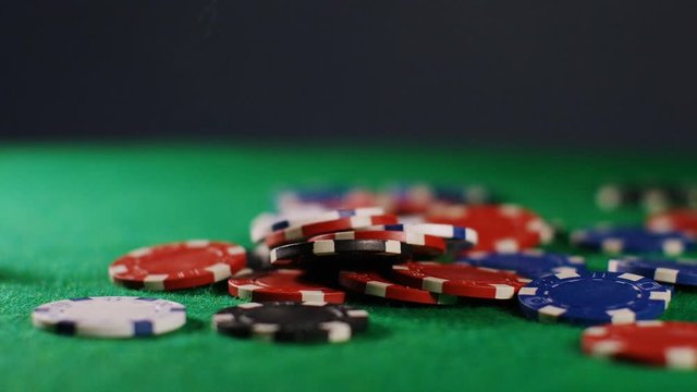 4K Colorful poker chips falling onto green felt, in slow motion