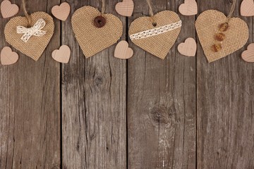 Top border of handmade burlap hearts with ribbon and buttons over a rustic wooden background