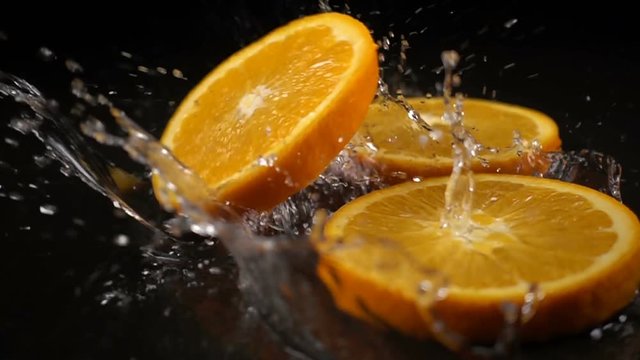 orange slices fall on the black surface covered with water