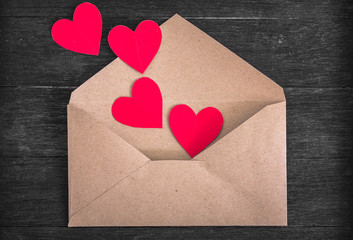 Brown envelope with red paper hearts on wood background