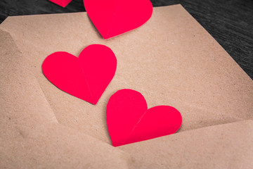 Brown envelope with red paper hearts on wood background