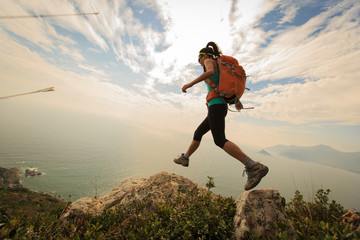 successful hiker jumping on seaside mountain peak rock