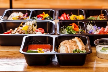 Healthy food and diet concept, restaurant dish delivery. Take away of fitness meal. Weight loss nutrition in foil boxes. Steamed veal with cous and vegetables at wood