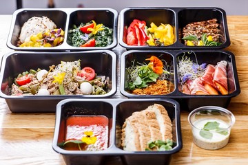 Healthy food and diet concept, restaurant dish delivery. Take away of fitness meal. Weight loss nutrition in foil boxes. Steamed veal with cous and vegetables at wood