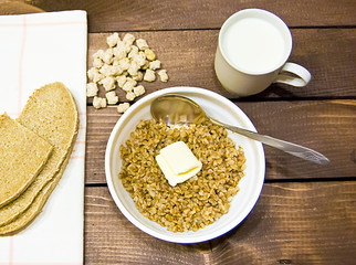 buckwheat with butter and milk in a glass, sliced bread on a wooden background