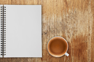 Blank notepad and coffee cup on wooden table.