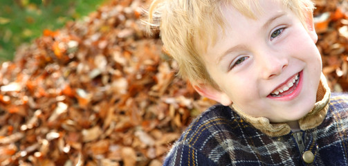 Smiling boy by a pile of leaves