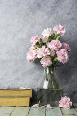 Pink carnation flowers in clear bottle and old book