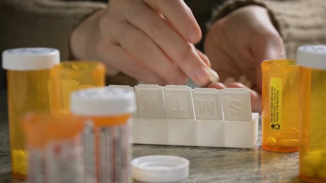 Female puts prescription pills into pill organizer in her kitchen. 