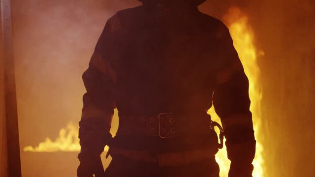 Portrait Shot of A Brave Fireman Standing in a Burning Building Fire Raging Behind Him. Open Flames and Smoke in the Background.  Shot on RED EPIC (uhd).