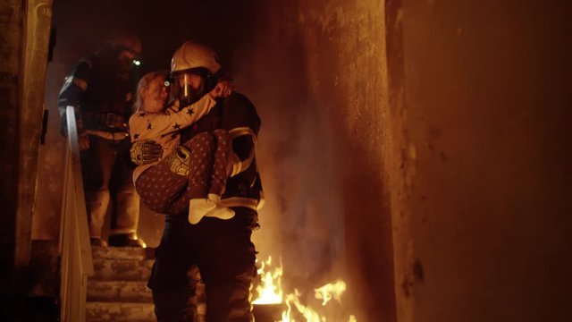 Burning Building. Group Of Firemen Descend on Burning Stairs. One Fireman Holds Saved Girl in His Arms.  Shot on RED EPIC (uhd).