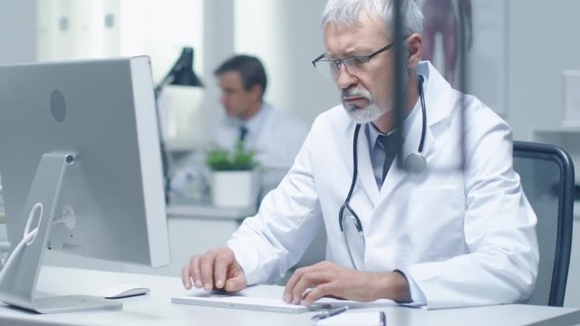 Close-up of a Senior Doctor and His Assistant Working at Desktop Computers. Sitting in Brightly Lit Office.  Shot on RED Cinema Camera in 4K (UHD).