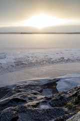 Snowy rock by a frozen and snowy lake in Finland at morning in the winter.
