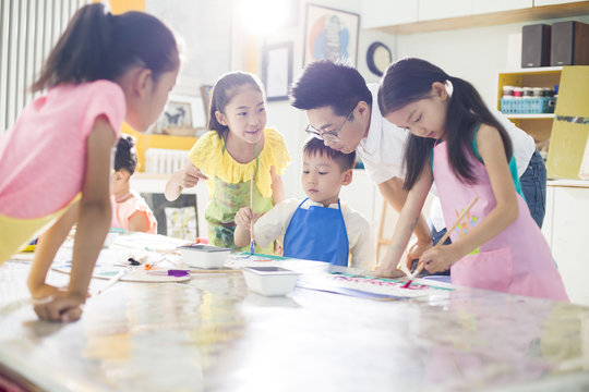 Little children painting in art class with teacher