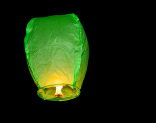 Green paper lantern floating into dark sky