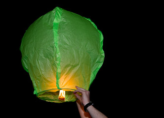 Green paper lantern being released into dark sky