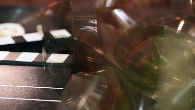 Panning shot left to write on vintage movie symbol objects, starting with clapper board, unrolled filmstrip and ending on 35mm cinema film reel