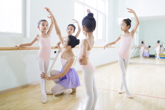 Young ballet instructor teaching girls in ballet studio