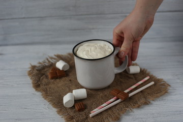 Hot chocolate with  caramel, whipped cream and marshmallow in white vintage cups on the wooden table.