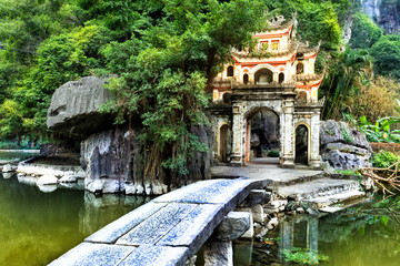 Outdoor park landscape with lake and stone bridge. Gate entrance to ancient Bich Dong pagoda complex. Ninh Binh, Vietnam travel destination.