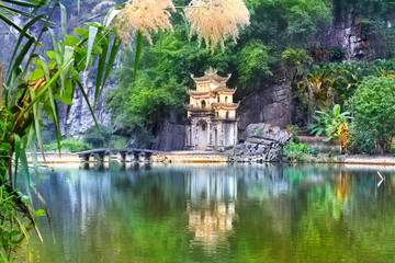 Outdoor park landscape with lake and stone bridge. Gate entrance to ancient Bich Dong pagoda complex. Ninh Binh, Vietnam travel destination.
